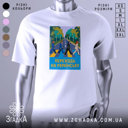Футболка переходь на українську, біла, зображена на манекені, фон світло-сірий, принт з п'ятьма персонажами, що переходять дорогу, на фоні зелених дерев і синього неба, текст "ПЕРЕХОДЬ НА УКРАЇНСЬКУ" у жовтому кольорі.