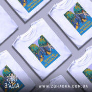 Футболка переходь на українську, біла, зображена на манекені, фон світло-сірий, принт з п'ятьма персонажами, що переходять дорогу, на фоні зелених дерев і синього неба, текст "ПЕРЕХОДЬ НА УКРАЇНСЬКУ" у жовтому кольорі.