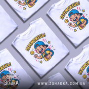 Футболка переможець для дітей. Біла футболка з яскравим принтом, на якому зображений хлопчик у блакитній кепці, що радісно піднімає руку. На фоні кольорові зірочки та усміхнене сонечко. Футболка представлена на манекені з нейтральним фоном.