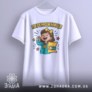 Футболка переможниця білого кольору, підвішена на вішалці, з принтом дівчинки з медаллю та подушкою, фон світло-сірий, деталі принта яскраві.