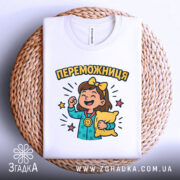 Футболка переможниця білого кольору, складена на плетеній кошику, з принтом дівчинки з медаллю та подушкою, фон білий, деталі принта яскраві.