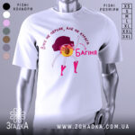 Футболка персик курага багіня, біла футболка на манекені, з принтом жовтого персика з рожевими чоботами та чорним волоссям, фон світло-сірий, текст червоним кольором.