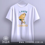 Футболка пес на кардіо, біла, підвішена на вішалці, фон світло-сірий, принт з жовтим текстом "I HATE CARDIO" та малюнком собаки на велотренажері.