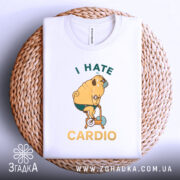 Футболка пес на кардіо, біла, складена на плетеній кошику, фон світло-сірий, принт з жовтим текстом "I HATE CARDIO" та малюнком собаки на велотренажері.