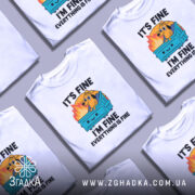 Футболка песик все добре. Біла футболка з принтом, зображення з ракурсу спереду, фон нейтральний. Принт містить жовтуватий фон з вогнем, собаку на сміттєвому контейнері, текст "IT'S FINE I'M FINE EVERYTHING IS FINE".