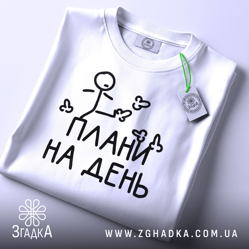 Футболка плани на день, білого кольору, зображена зверху, складена на білому фоні, принт з малюнком stickman і написом "ПЛАНИ НА ДЕНЬ" чорного кольору, на комірці видно етикетку з зеленим шнурком.