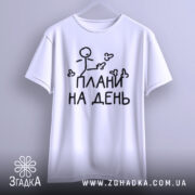 Футболка плани на день, білого кольору, підвішена на вішалці, фон світло-сірий, принт з малюнком stickman і написом "ПЛАНИ НА ДЕНЬ" чорного кольору, видно округлі краї рукавів.