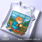 Футболка почну з понеділка, біла, розкладена на поверхні, фон світло-сірий, принт з котом у халаті, що тримає чашку, з елементами декору на задньому плані.