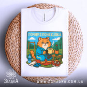 Футболка почну з понеділка, біла, складена на плетеній основі, фон світлий, принт з котом у халаті, що тримає чашку, з елементами декору на задньому плані.