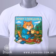 Футболка почну з понеділка, біла, розкладена на поверхні, фон світло-сірий, принт з котом у халаті, що тримає чашку, з елементами декору на задньому плані.