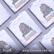 Футболка подарунків захотілося, біла, зображена з фронтального ракурсу, на фоні світло-сірого кольору, принт зображає кота в червоній шапці, обмотаного гірляндою з лампочок, з текстом "МЕНІ ПОДАРУНКІВ ЗАХОТІЛОСЯ".