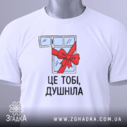 Футболка подарунок душнілі, біла, зображена зверху, на ній видно етикетку з зеленим шнурком, фон світло-сірий, принт з малюнком вікна з червоною стрічкою та написом 'ЦЕ ТОБІ, ДУШНІЛА'.