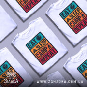 Футболка подорожуй легко, біла, зображена на манекені з правого боку, фон світло-сірий, принт з написом 'EAT SLEEP CAMP REPEAT' у яскравих кольорах: бірюзовий, оранжевий, жовтий та червоний.