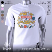 Футболка покликання вчителя білого кольору, зображена з близького ракурсу, фон нейтральний, принт містить текст "ВЧИТЕЛЬ НЕ РОБОТА, А ПОКЛИКАННЯ" з ілюстраціями олівців, яблука та книжки.