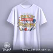 Футболка покликання вчителя білого кольору, підвішена на вішалці, фон світло-сірий, принт з текстом "ВЧИТЕЛЬ НЕ РОБОТА, А ПОКЛИКАННЯ" з кольоровими малюнками олівців і яблука.