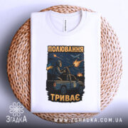 Футболка полювання триває, біла футболка складена на плетеній основі, фон світлий, принт з військовим на пікапі, з вибухами та літаком на фоні.