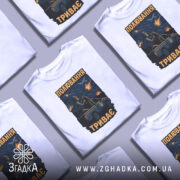 Футболка полювання триває, біла футболка на манекені, фон світло-сірий, принт з зображенням військового з кулеметом на пікапі, на фоні літака та вибухів.