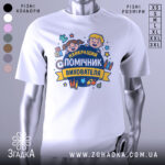 Футболка помічник вихователя, біла, зображена з правого ракурсу на манекені, фон світло-сірий, принт з веселими дітьми та текстом 'НАЙКРАЩИЙ ПОМІЧНИК ВИХОВАТЕЛЯ' у яскравих кольорах.