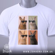 Футболка попарт кролики, біла, складена на поверхні, фон білий, принт з чотирма кроликами в окулярах, два з них коричневі, два світлі, з тегом на зеленому шнурку.