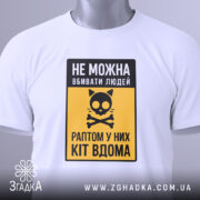 Футболка попередження про кота, біла, складена на поверхні, фон світло-сірий, принт з чорним написом і жовтим фоном, з малюнком кота і кісток, з етикеткою на зеленому шнурку.
