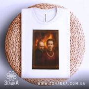 Футболка портрет українські класики, біла, складена на плетеній основі, фон з теплими відтінками, принт з портретами двох осіб, один з них у темному одязі, інший у червоній сорочці з намистом, видима етикетка на горловині.