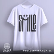 Футболка посміхнись. Біла футболка на вішалці, фон світло-сірий, принт з написом 'SMILE' з усмішкою, видно округлі краї рукавів.