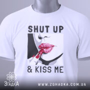 Футболка поцілуй мене, біла, зображена зверху, фон світло-сірий, принт з червоними губами та помадою, текст "SHUT UP & KISS ME", на комірці є етикетка.