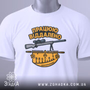 Футболка працюю віддалено, білого кольору, складена на поверхні, фон світло-сірий, принт з написом 'ПРАЦЮЮ ВІДДАЛЕНО' та зображенням гвинтівки і вимірювальної лінійки в жовтих і чорних кольорах, з етикеткою на зеленому шнурку.