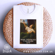 Футболка прекрасний день. Біла футболка, складена на плетеній основі, з принтом жінки, що тримає птаха. Принт займає центральну частину, знизу напис: 'Який прекрасний блаженний день'.