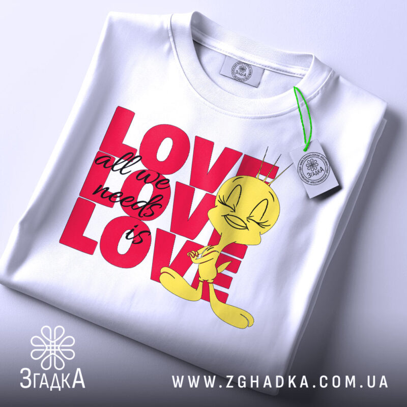 Футболка про кохання, білого кольору, складена на поверхні, фон світлий, принт з жовтою пташкою та написом 'LOVE all we need is LOVE' у червоному кольорі, на футболці є етикетка.