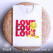 Футболка про кохання, білого кольору, складена на плетеній основі, фон світлий, принт з жовтою пташкою та написом 'LOVE all we need is LOVE' у червоному кольорі.