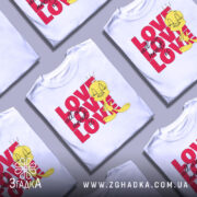 Футболка про кохання, білого кольору, зображена на манекені, фон нейтральний, принт містить жовту пташку з написом 'LOVE all we need is LOVE' у червоному кольорі.