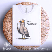 Футболка проблемний голуб, біла, складена на плетеній кошику, фон світлий, принт з пташкою з ножем і текстом 'ANY PROBLEMS?'.
