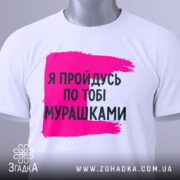 Футболка пройдусь мурашками, біла, зображена на столі, фон світлий, принт у вигляді рожевої смуги з текстом чорного кольору, на комірці є етикетка.