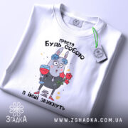 Футболка просто будь собою, білого кольору, зображена в плоскому вигляді, фон світлий, принт з малюнком зайця з квітами та келихом, текст зверху на українській мові, на комірці видно етикетку.