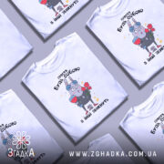 Футболка просто будь собою, білого кольору, зображена на манекені з блискучою поверхнею, фон нейтральний, принт з малюнком зайця з квітами та келихом, текст зверху на українській мові.