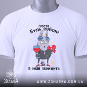 Футболка просто будь собою, білого кольору, зображена в плоскому вигляді, фон світлий, принт з малюнком зайця з квітами та келихом, текст зверху на українській мові, на комірці видно етикетку.