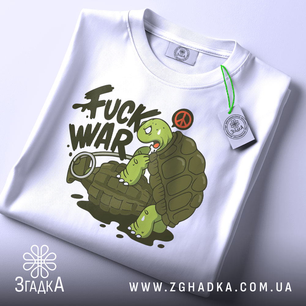 Футболка проти війни. Біла футболка, складена на столі, з принтом черепахи на гранаті. Принт яскравий, з написом 'FUCK WAR' та символом миру, з етикеткою на зеленому шнурку.