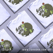 Футболка проти війни. Біла футболка на манекені, з принтом черепахи, що сидить на гранаті. Принт виконаний у зелених та чорних тонах, з написом 'FUCK WAR' і символом миру.