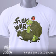 Футболка проти війни. Біла футболка, складена на столі, з принтом черепахи на гранаті. Принт яскравий, з написом 'FUCK WAR' та символом миру, з етикеткою на зеленому шнурку.