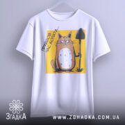 Футболка прийшов час копати. Біла футболка, підвішена на вішалці, з принтом кота з лопатою на жовтому фоні. Принт чіткий, з виразним обличчям кота, фон нейтральний, що акцентує увагу на малюнку.