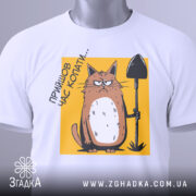Футболка прийшов час копати. Біла футболка, складена на поверхні, з видимим принтом кота з лопатою на жовтому фоні. Принт розташований в центрі, а на комірці видно етикетку. Фон світлий, що підкреслює деталі принта.