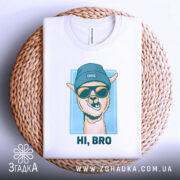 Футболка прикольна лама, біла, складена на плетеному кошику, зображена з верхнього ракурсу, фон світло-сірий, принт з ламою в блакитній шапці та окулярах, текст "HI, BRO" під малюнком.