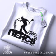 Футболка принц пенсії, біла, складена на поверхні, фон світло-сірий, принт чорного кольору з силуетом людини, що кидає пісок, текст "ПЕНСІЯ" великими літерами, на комірці видна етикетка.