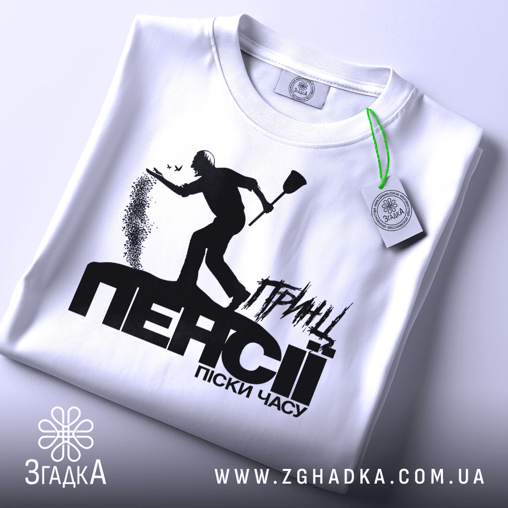 Футболка принц пенсії, біла, складена на поверхні, фон світло-сірий, принт чорного кольору з силуетом людини, що кидає пісок, текст "ПЕНСІЯ" великими літерами, на комірці видна етикетка.