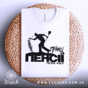 Футболка принц пенсії, біла, складена на плетеній кошику, фон світло-сірий, принт чорного кольору з силуетом людини, що кидає пісок, текст "ПЕНСІЯ" великими літерами.