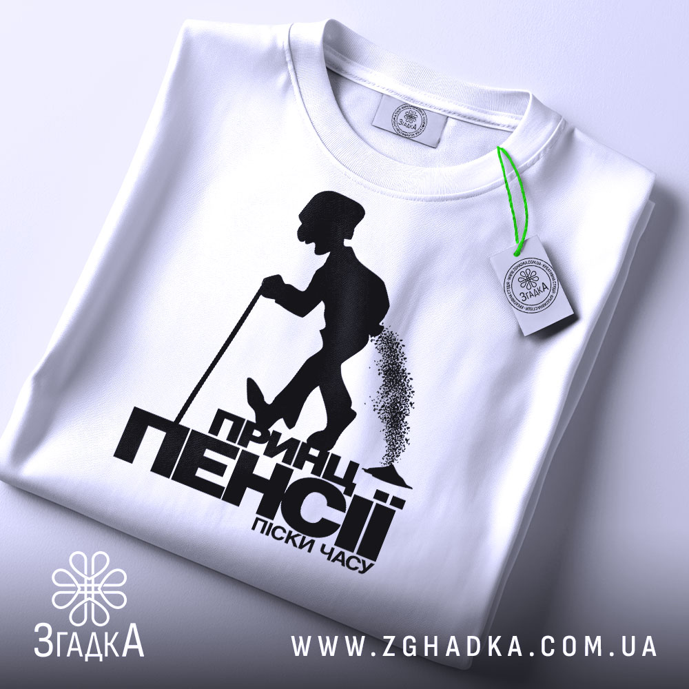 Футболка принц пенсії, біла, зображена зверху, складена на поверхні, фон світлий, принт чорного кольору з силуетом постаті, що йде з палицею, з етикеткою зеленого кольору.
