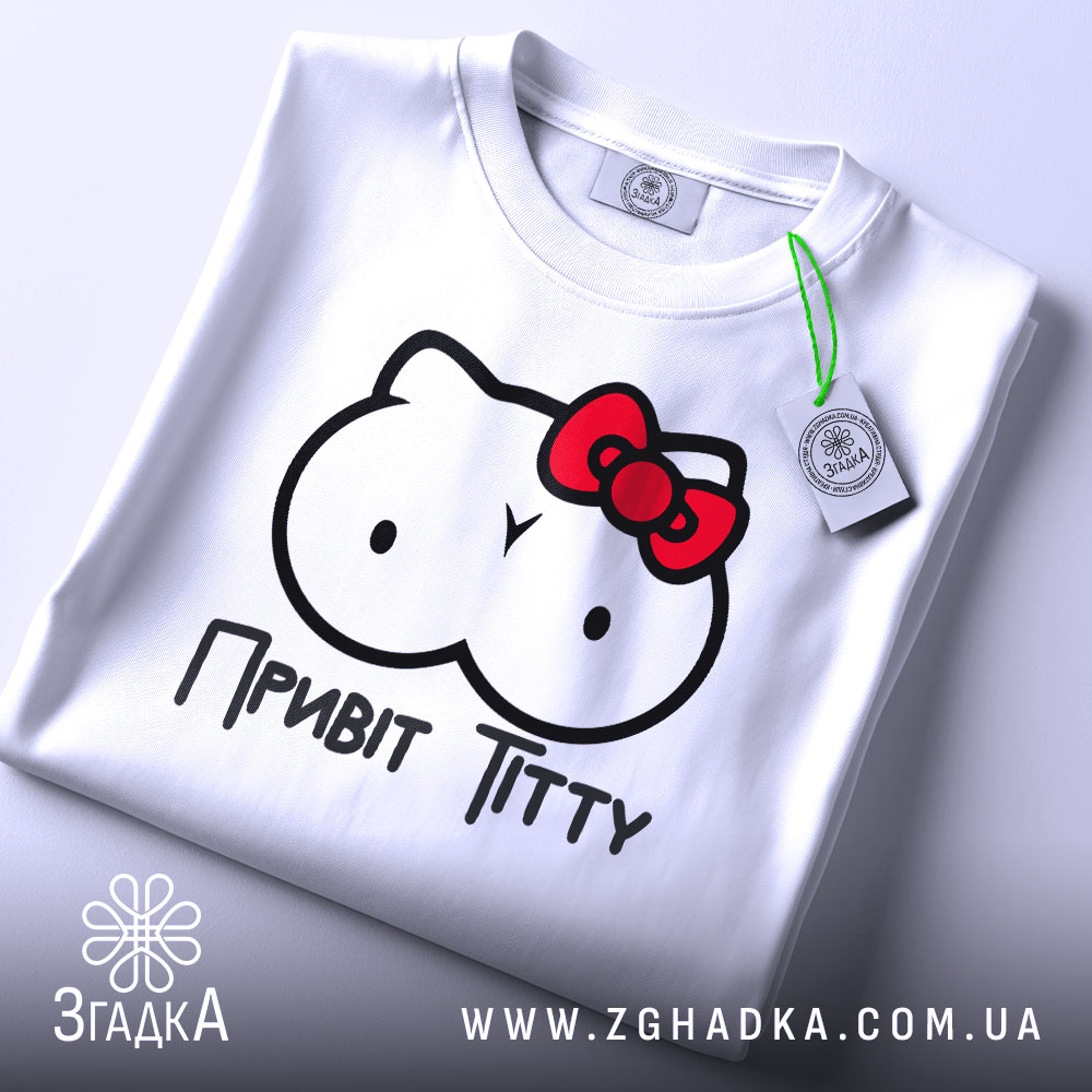 Футболка привіт ціці, біла, зображена на столі, ракурс зверху, фон світлий, принт з малюнком у вигляді двох круглих форм з очима та червоною бантиком, текст "Привіт Тітті" під малюнком, на футболці є етикетка.
