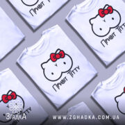 Футболка привіт ціці, біла, зображена на манекені, фон нейтральний, принт з малюнком у вигляді двох круглих форм з очима та червоною бантиком, текст "Привіт Тітті" під малюнком.