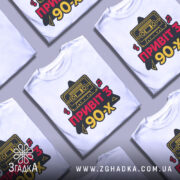 Футболка привіт з 90-х, біла, зображена на манекені, фон світло-сірий, принт з касетою та написом 'ПРИВІТ З 90-х' у червоному та жовтому кольорах.